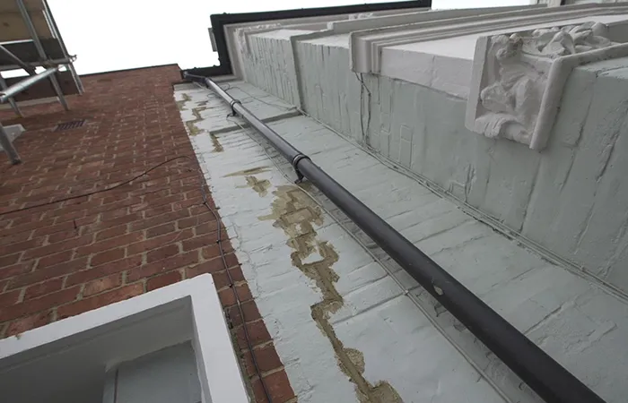 Drainage pipe along a building wall showing signs of water damage and repair work, highlighting the importance of professional drainage services for property maintenance.