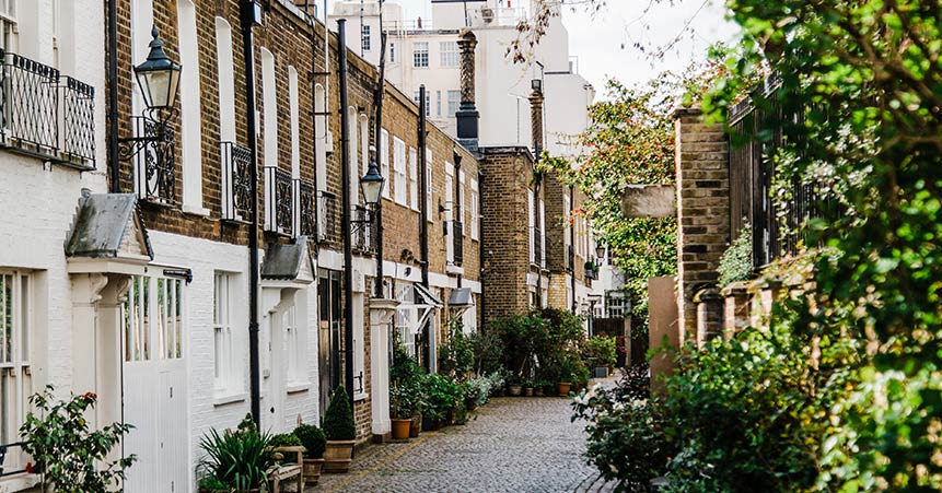 Charming residential street in Barnes, London, featuring brick and white-washed houses with balconies, surrounded by greenery and potted plants, illustrating the local area serviced by Environ Drainage Services.