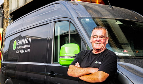 Man standing confidently next to Environ Drainage Services van, showcasing the company's branding and contact information, emphasizing professional drainage solutions in London.