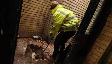 Engineer in high-visibility jacket performing drain cleaning in a stadium facility, emphasizing emergency drainage services and maintenance.