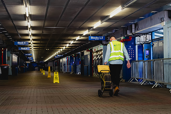 Maintenance worker pushing a cart in a stadium corridor, with caution signs and directional signage for blocks, highlighting the importance of drain cleaning services for large events.