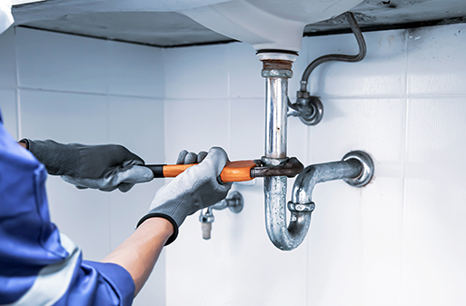 Plumber using a wrench to repair drainage pipes, illustrating professional plumbing services related to drain issues and maintenance.
