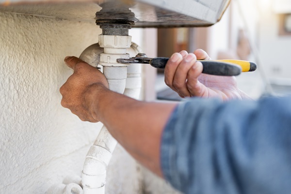 Plumber using a wrench to repair a drainage pipe, highlighting professional blocked drain services in London.