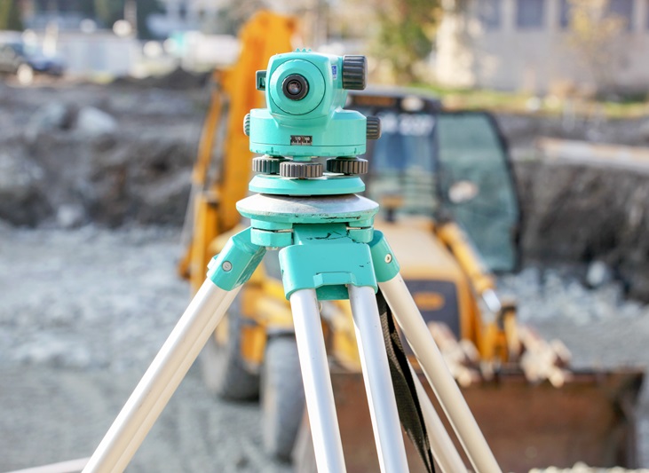 Surveying equipment in foreground with construction machinery in background, representing advanced technology used by drainage contractors in London.